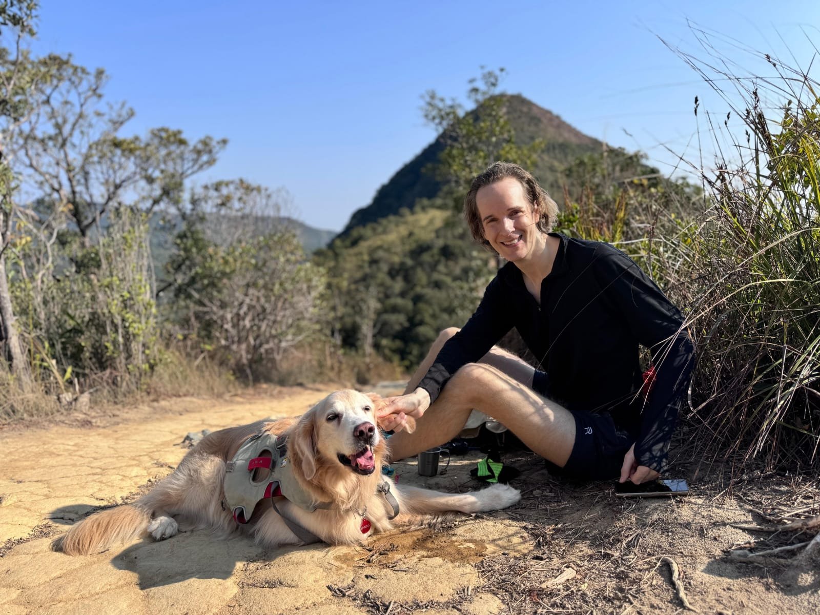 Felix Nikolas Prehn resting on a hillside trail with a golden retriever