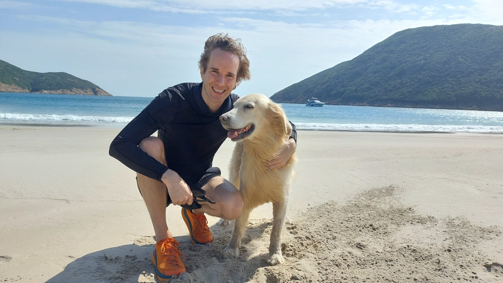 Nikolas Prehn (Felix Nikolas Prehn), crouching on a sandy beach with his golden retriever Winston
