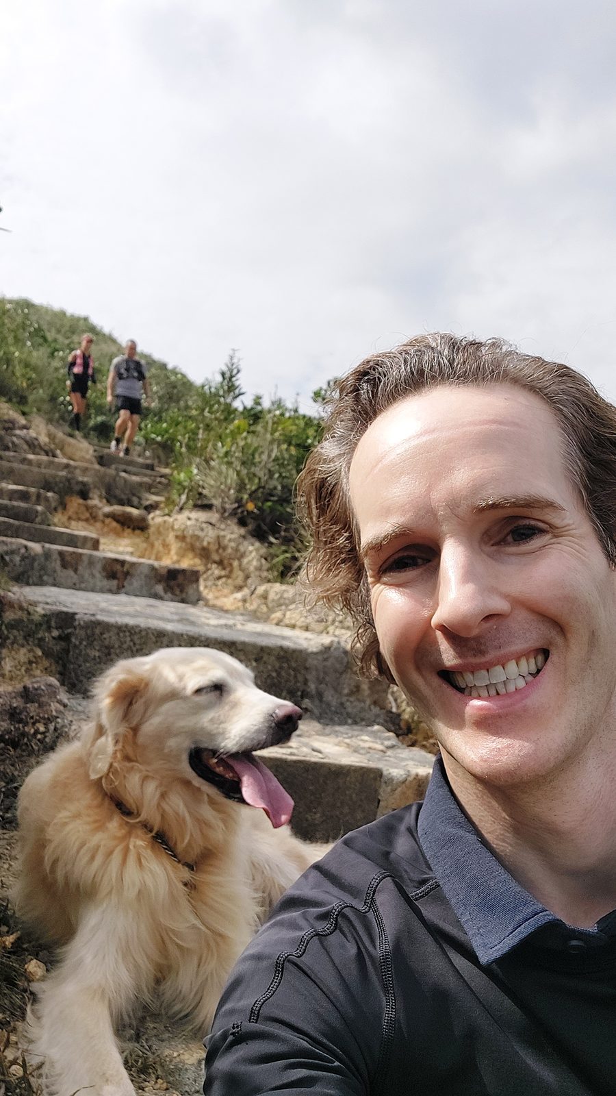 Nikolas Prehn (Felix Nikolas Prehn), on a stone path along a coastal trail with his golden retriever Winston
