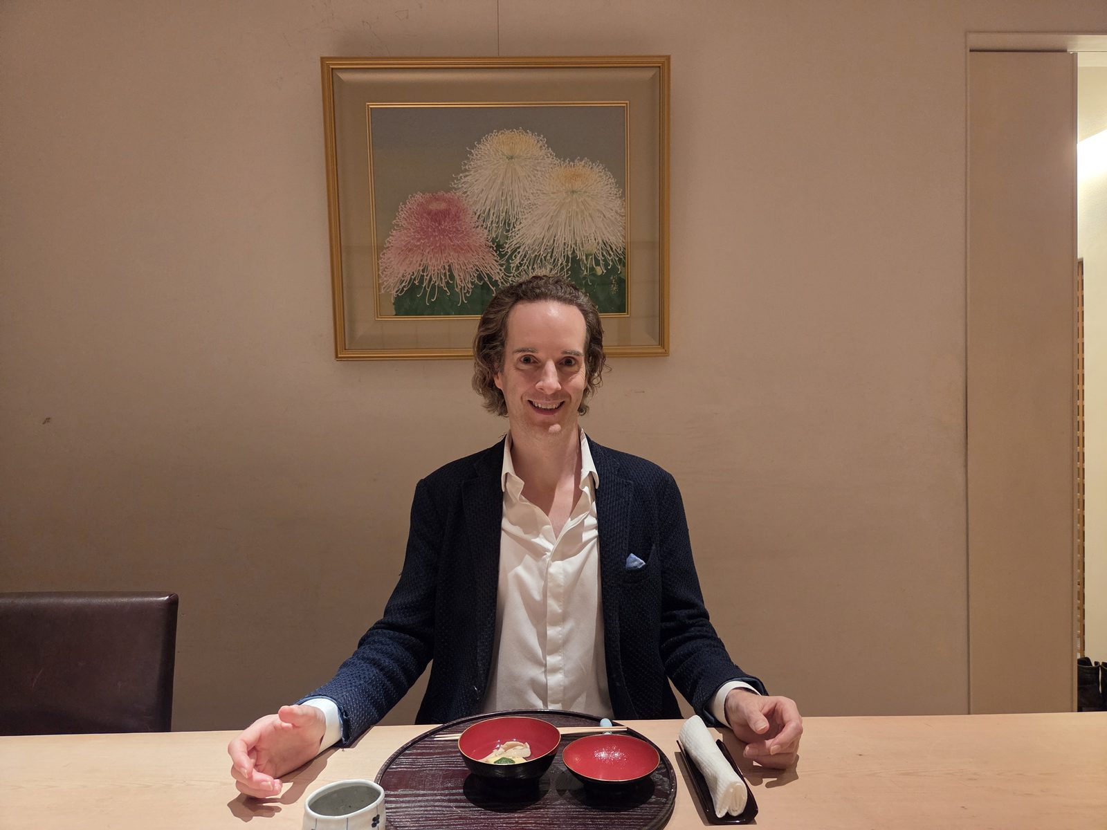 Nikolas Prehn (Felix Nikolas Prehn), in a navy knit jacket at a restaurant counter beneath a chrysanthemum painting