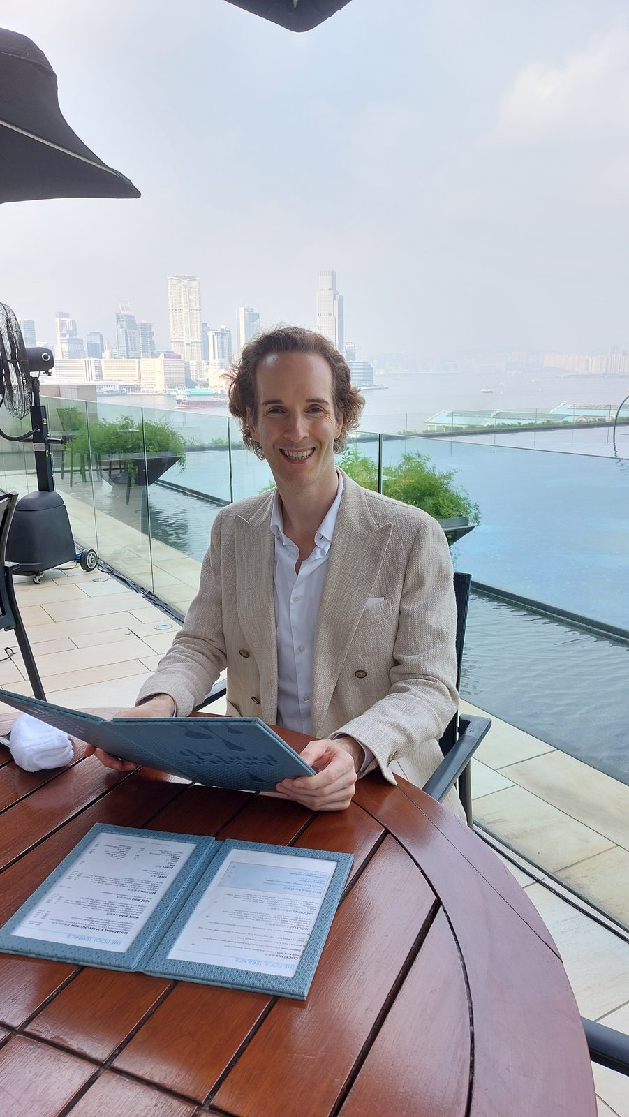 Nikolas Prehn (Felix Nikolas Prehn), in a linen jacket on a rooftop pool terrace with the skyline behind