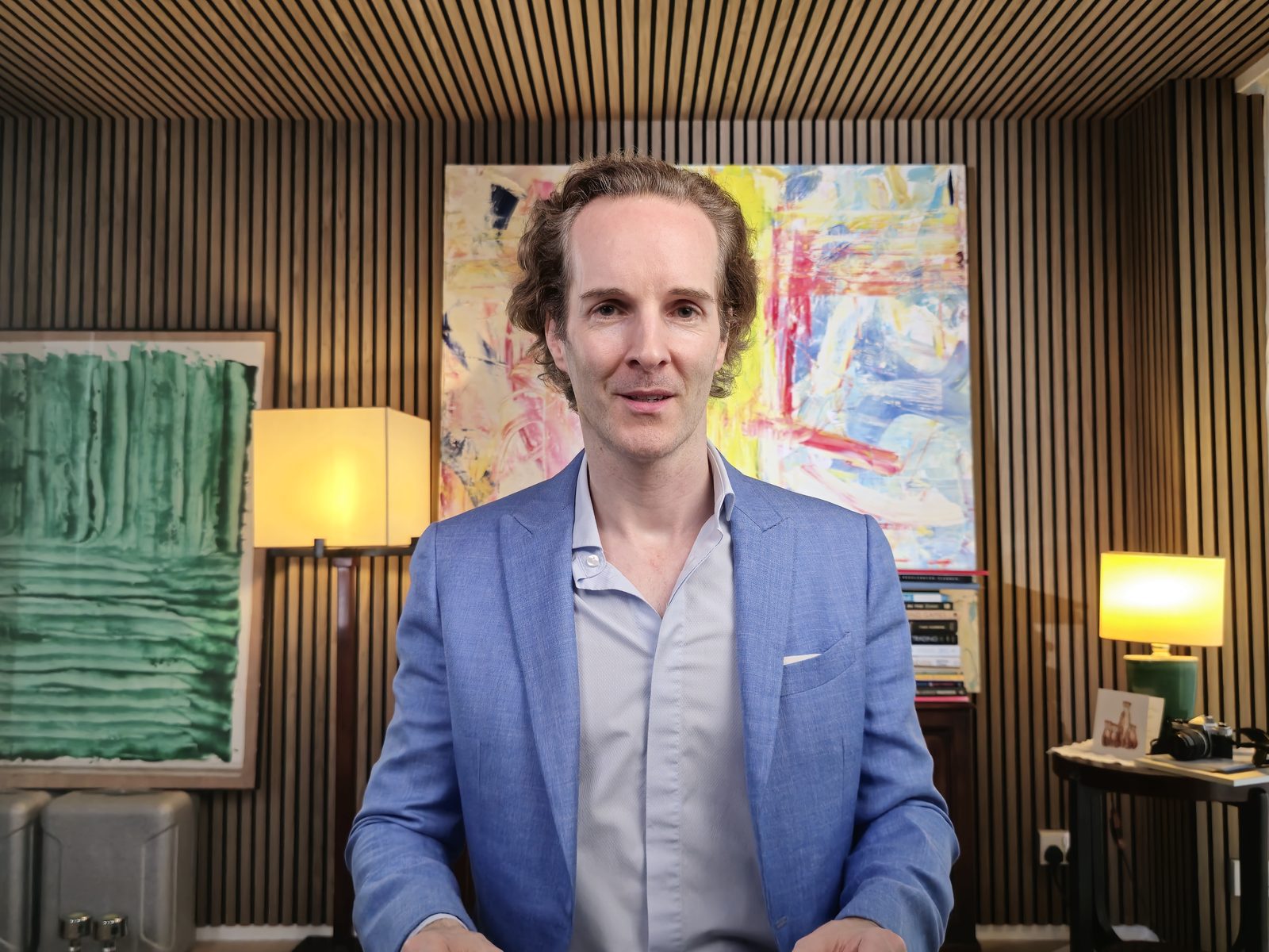 Nikolas Prehn (Felix Nikolas Prehn), in a blue blazer seated in a study with abstract paintings