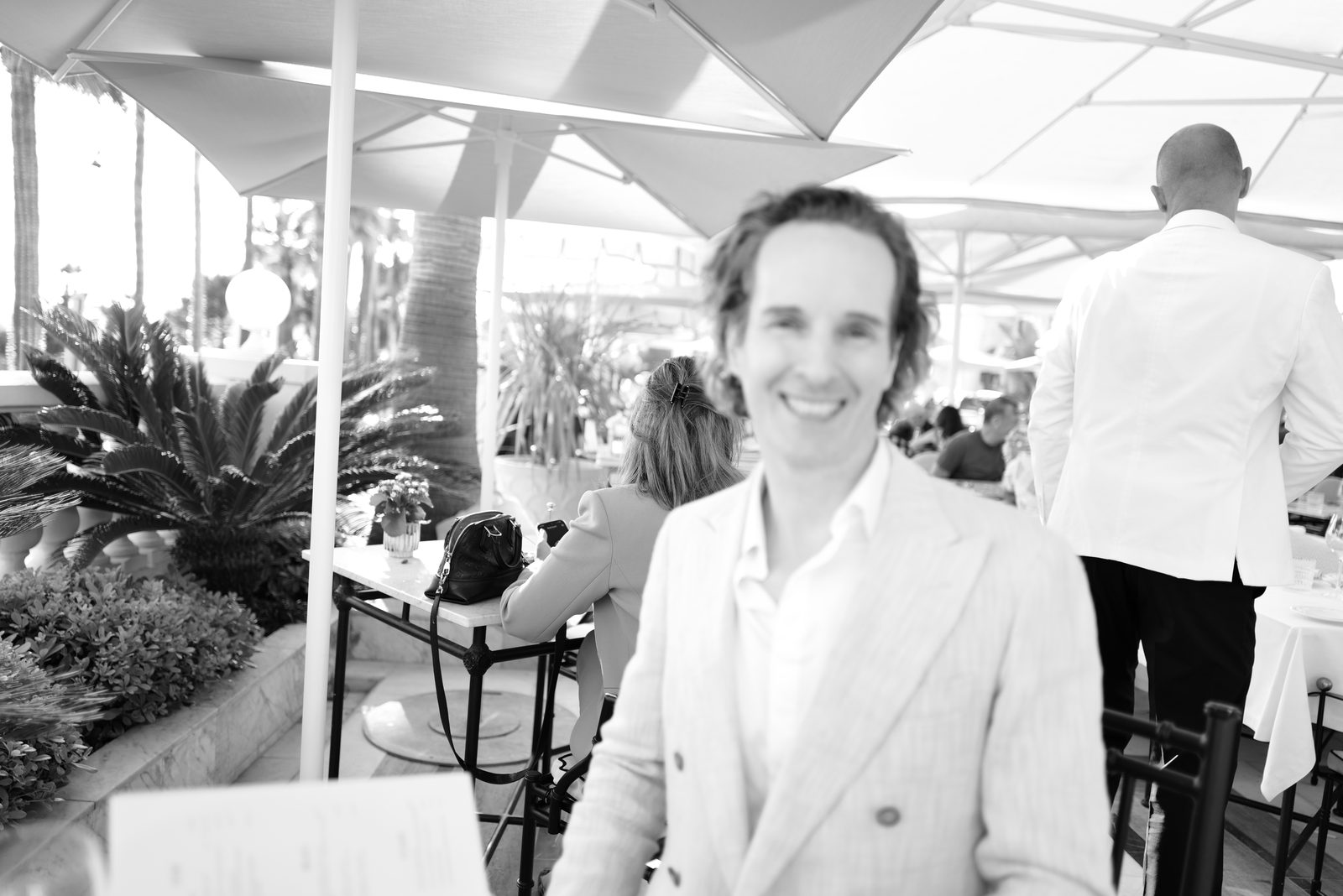 Nikolas Prehn (Felix Nikolas Prehn), in a linen double breasted jacket at a terrace cafe under parasols, black and white